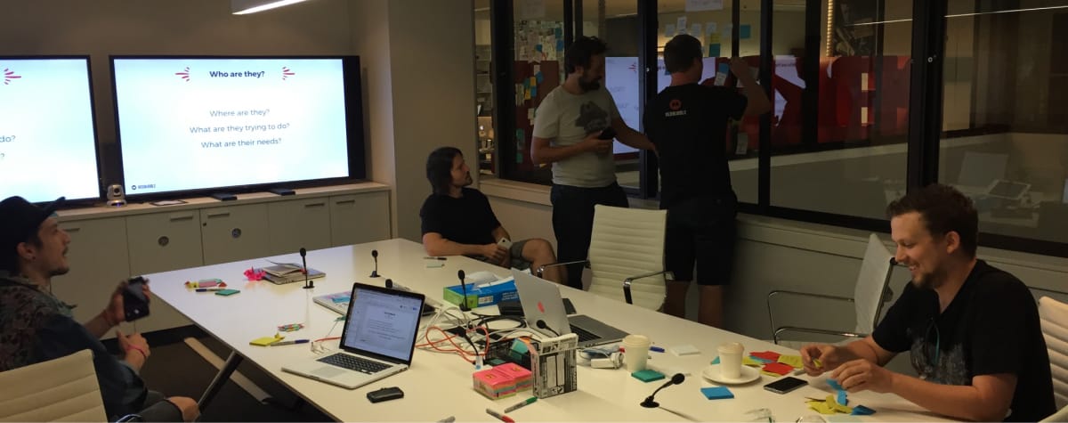team collaborating in office space in front of screens and whiteboard